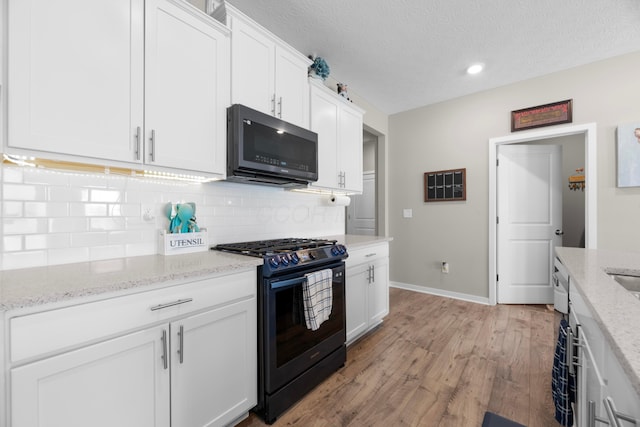 kitchen featuring light stone counters, gas stove, and white cabinets