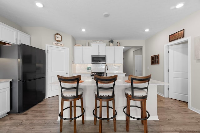 kitchen featuring white cabinetry, backsplash, stainless steel appliances, and an island with sink