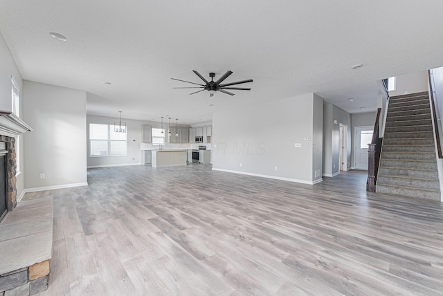 unfurnished living room with ceiling fan with notable chandelier, a textured ceiling, a fireplace, and light hardwood / wood-style flooring