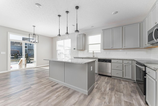 kitchen with sink, gray cabinetry, stainless steel appliances, a kitchen island, and decorative light fixtures