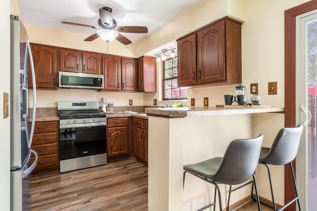 kitchen with appliances with stainless steel finishes, a breakfast bar, hardwood / wood-style floors, and kitchen peninsula