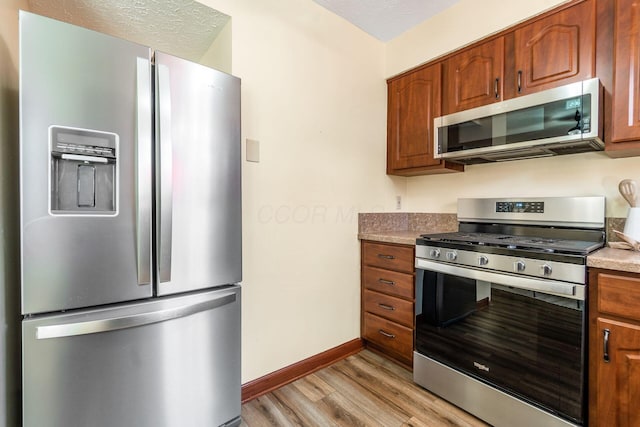 kitchen featuring stainless steel appliances, a textured ceiling, and light wood-type flooring