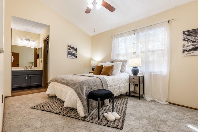 carpeted bedroom with ceiling fan, lofted ceiling, ensuite bathroom, and sink