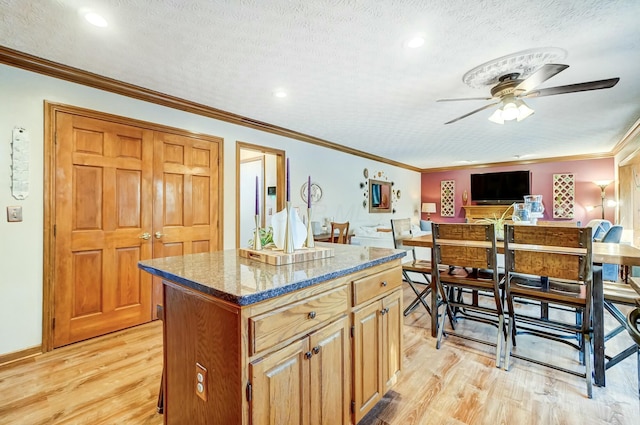 kitchen with ornamental molding, a center island, a textured ceiling, and light wood-type flooring