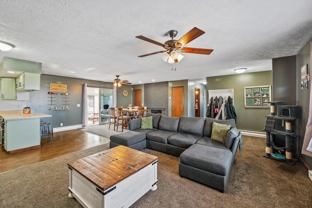 living room with a textured ceiling, a wood stove, a baseboard radiator, dark hardwood / wood-style flooring, and ceiling fan