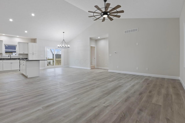 unfurnished living room with sink, ceiling fan with notable chandelier, high vaulted ceiling, and light wood-type flooring