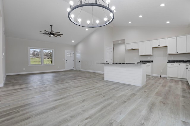 kitchen featuring white cabinetry, high vaulted ceiling, hanging light fixtures, dark stone countertops, and light hardwood / wood-style floors