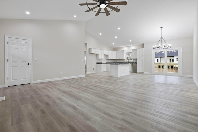 unfurnished living room with sink, light wood-type flooring, ceiling fan with notable chandelier, and high vaulted ceiling