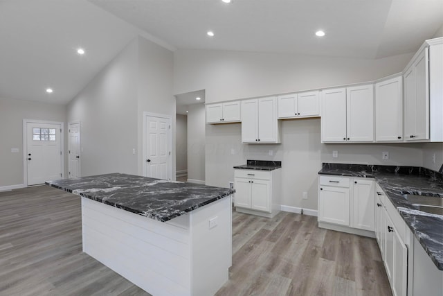 kitchen featuring light wood-type flooring, white cabinets, high vaulted ceiling, and dark stone counters