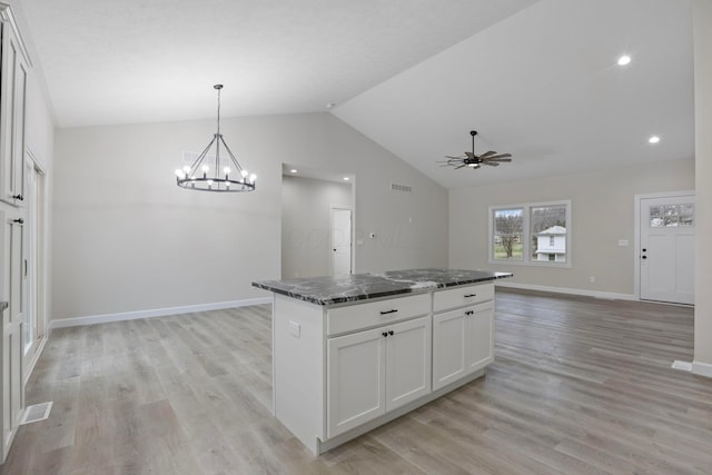 kitchen with lofted ceiling, white cabinetry, light hardwood / wood-style flooring, a kitchen island, and dark stone counters