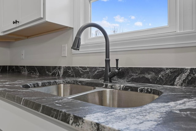 details with white cabinetry, sink, and dark stone countertops