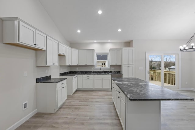 kitchen featuring sink, an inviting chandelier, a kitchen island, light hardwood / wood-style floors, and white cabinets