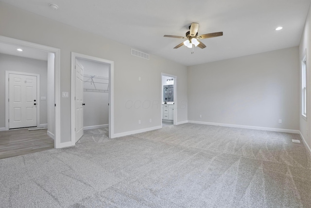 interior space featuring ceiling fan, ensuite bath, a spacious closet, and light carpet