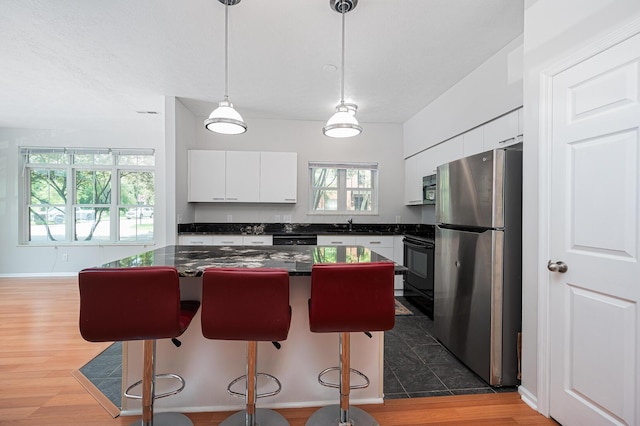 674 Park St, Columbus, OH 43215 - kitchen with freestanding refrigerator, dark countertops, white cabinets, black stove, and a kitchen bar