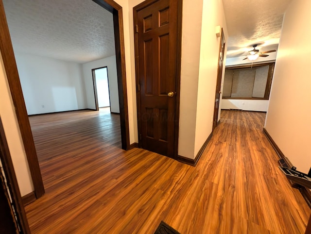 hall with a textured ceiling, wood finished floors, and baseboards