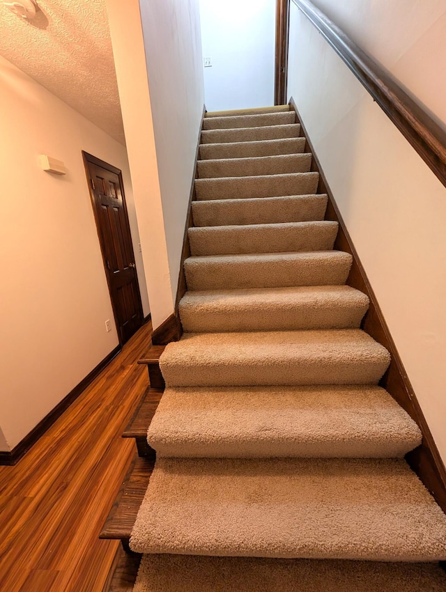 staircase featuring a textured ceiling, wood finished floors, and baseboards