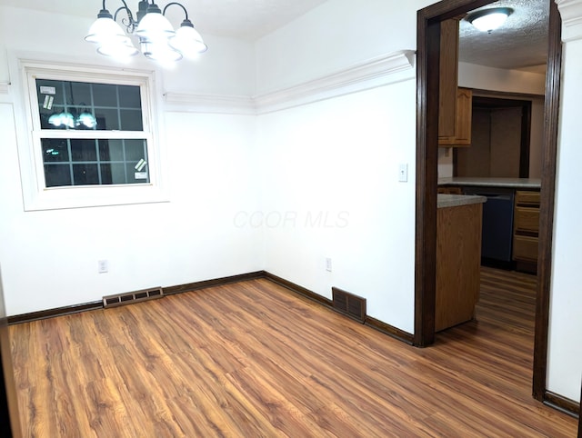 spare room featuring dark wood-style flooring, visible vents, and an inviting chandelier