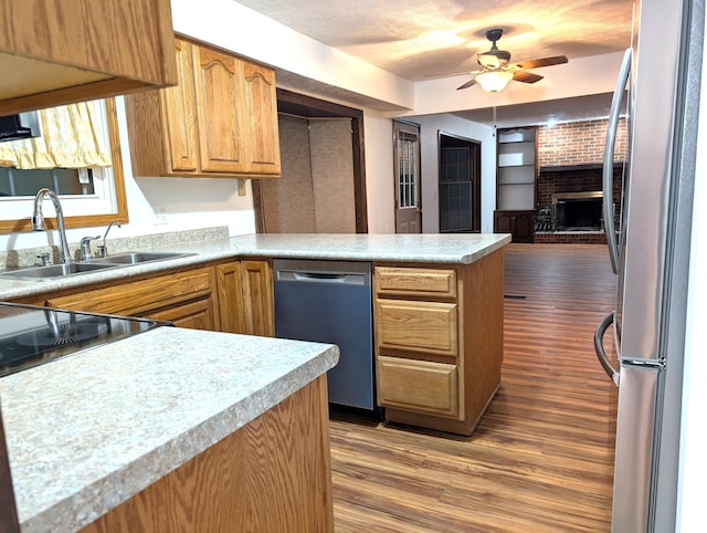 kitchen with stainless steel appliances, a brick fireplace, a sink, wood finished floors, and a peninsula