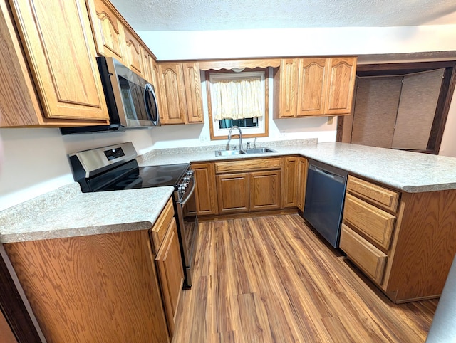 kitchen featuring a textured ceiling, a peninsula, wood finished floors, a sink, and appliances with stainless steel finishes