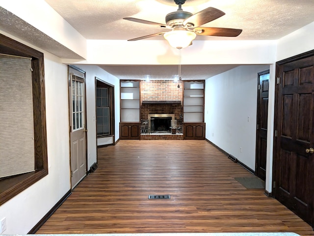 unfurnished living room with dark wood-style floors, a brick fireplace, baseboards, and a textured ceiling