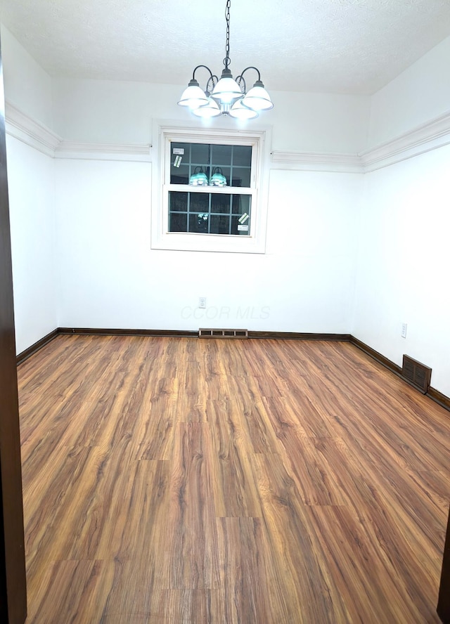 unfurnished room featuring a notable chandelier, visible vents, and wood finished floors