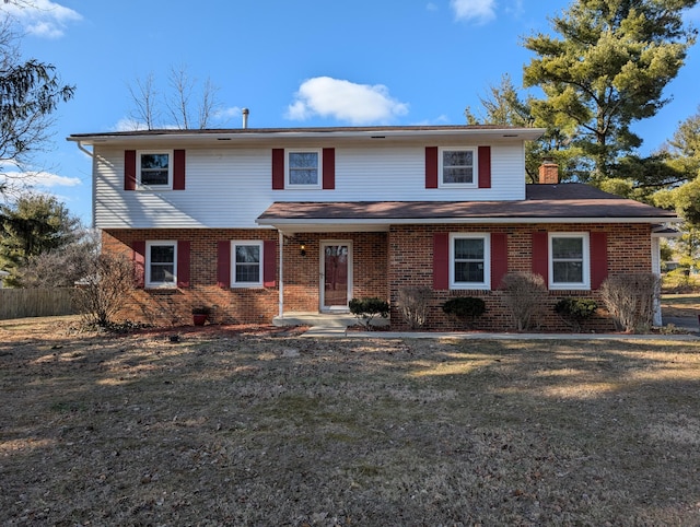 traditional-style house with brick siding, fence, a chimney, and a front lawn