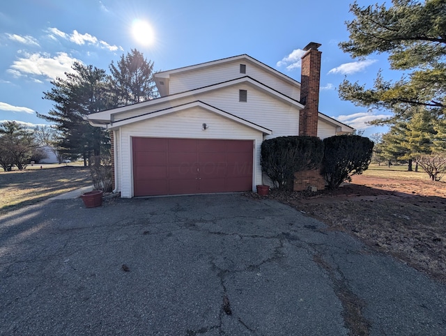 view of home's exterior with driveway, a chimney, and an attached garage