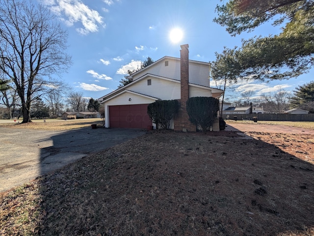 view of property exterior with a garage, aphalt driveway, a chimney, and fence