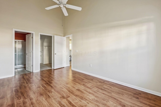 unfurnished bedroom with hardwood / wood-style floors, a spacious closet, ceiling fan, and a high ceiling