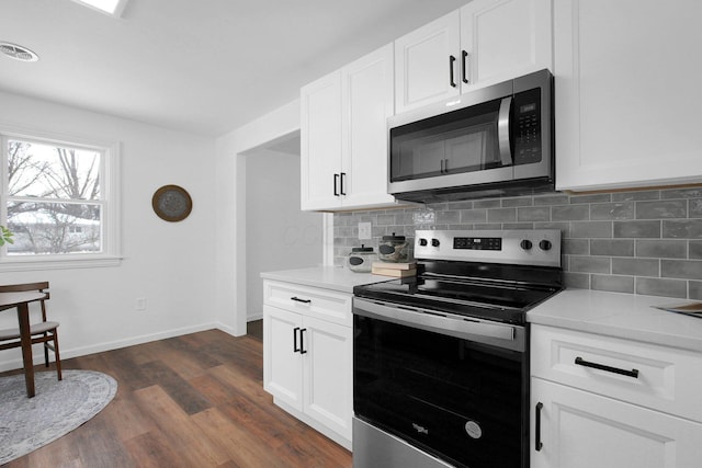 kitchen featuring white cabinetry, dark hardwood / wood-style floors, stainless steel appliances, light stone countertops, and backsplash