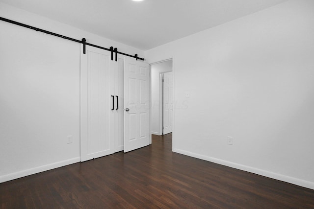 unfurnished bedroom featuring a barn door and dark hardwood / wood-style flooring