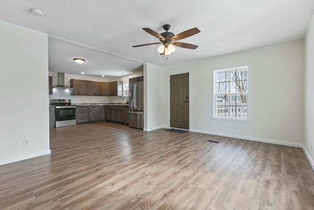 unfurnished living room with baseboards, ceiling fan, a textured ceiling, and light wood finished floors