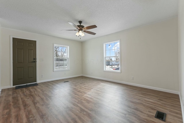 unfurnished room featuring dark wood finished floors, visible vents, a ceiling fan, a textured ceiling, and baseboards