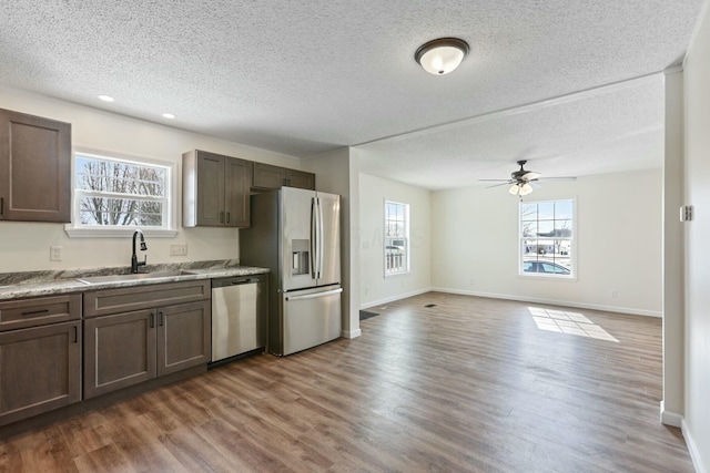 kitchen with appliances with stainless steel finishes, a sink, dark brown cabinets, and wood finished floors