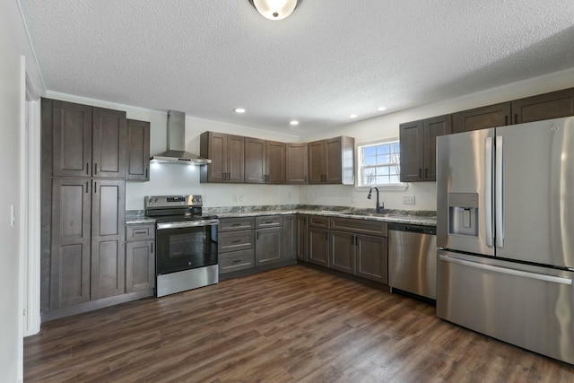 kitchen with stainless steel appliances, wall chimney range hood, dark wood-type flooring, and a sink