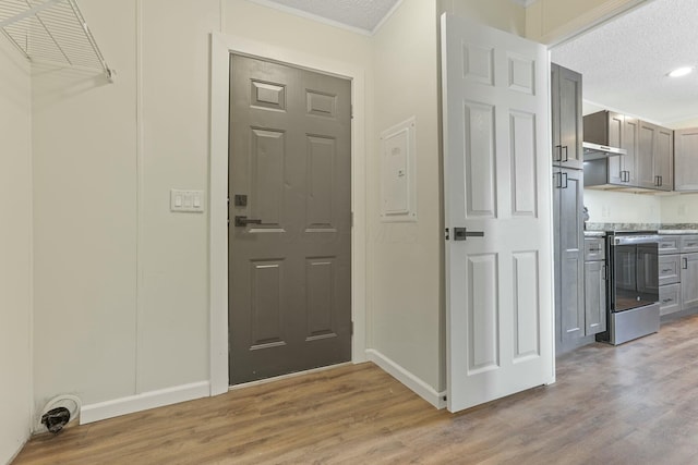 entryway with light wood finished floors, baseboards, ornamental molding, and a textured ceiling