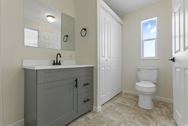 bathroom featuring a closet, toilet, vanity, a textured ceiling, and baseboards