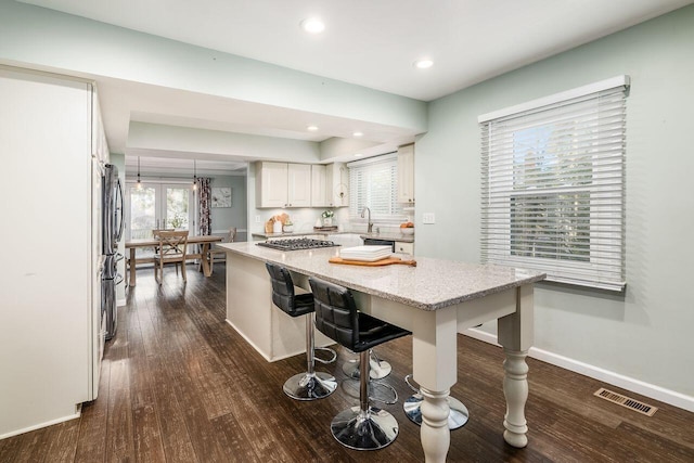 kitchen with pendant lighting, a breakfast bar area, white cabinetry, dark hardwood / wood-style floors, and light stone counters