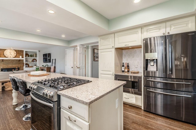 kitchen with a kitchen island, appliances with stainless steel finishes, dark hardwood / wood-style floors, light stone counters, and a brick fireplace