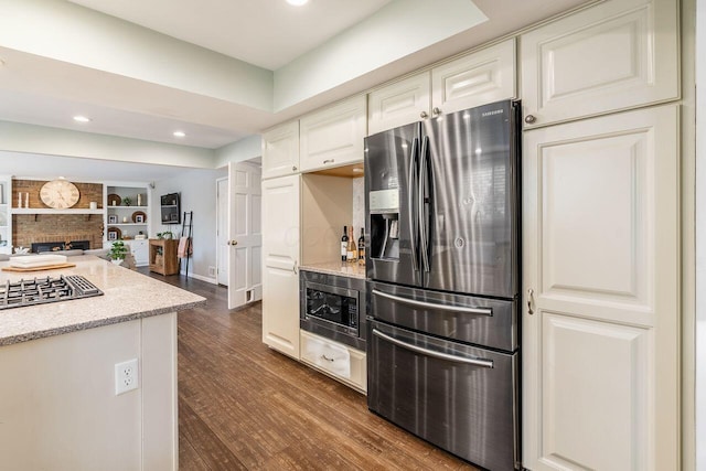 kitchen featuring dark hardwood / wood-style floors, built in features, a fireplace, stainless steel appliances, and light stone countertops