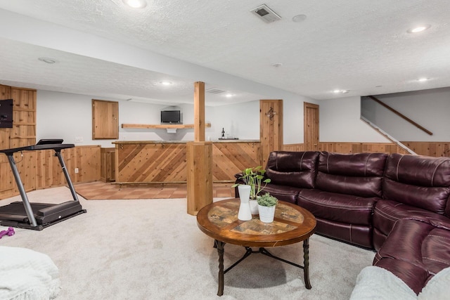 living room featuring light carpet, bar area, a textured ceiling, and wood walls