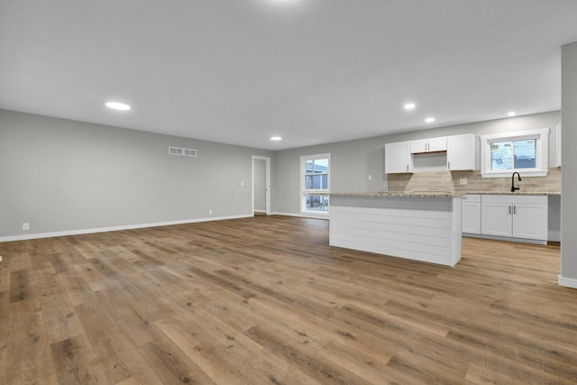 kitchen featuring tasteful backsplash, light wood-type flooring, light stone counters, and white cabinets