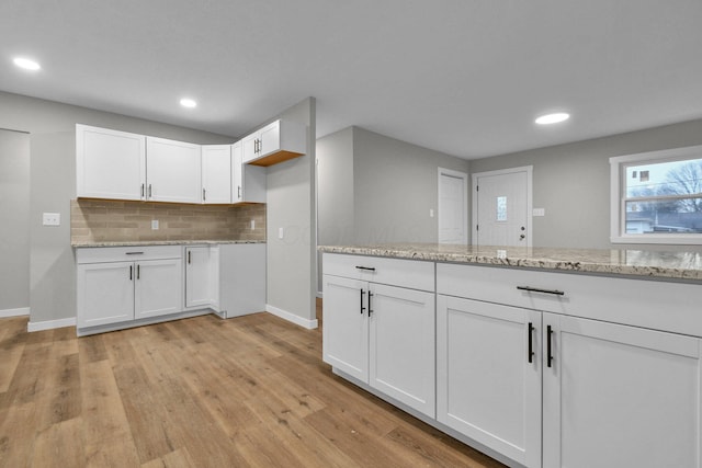 kitchen with white cabinetry, decorative backsplash, light hardwood / wood-style flooring, and light stone countertops