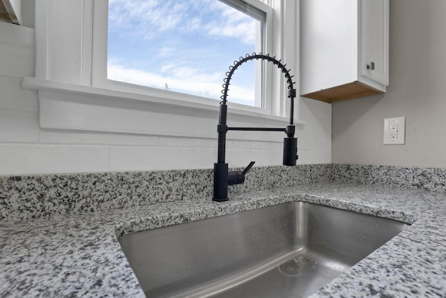 details featuring white cabinetry, light stone countertops, and sink