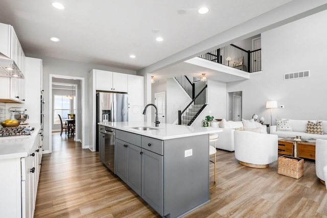 kitchen featuring sink, gray cabinetry, white cabinets, light hardwood / wood-style floors, and a center island with sink