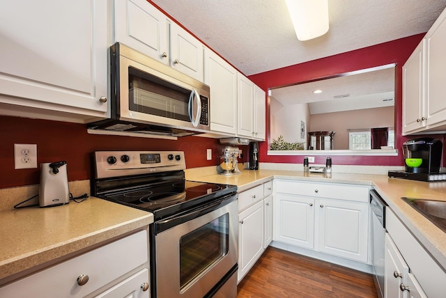 kitchen with a textured ceiling, dark wood-type flooring, stainless steel appliances, and white cabinets