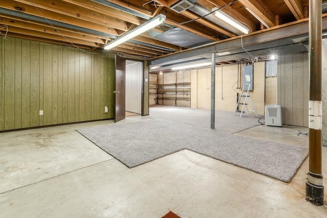 basement featuring electric panel and wooden walls