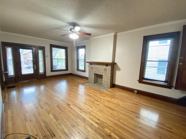 unfurnished living room with a tiled fireplace, ornamental molding, ceiling fan, and light hardwood / wood-style flooring