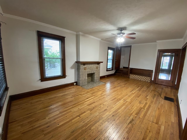 unfurnished living room with a tiled fireplace, ornamental molding, ceiling fan, and light hardwood / wood-style flooring