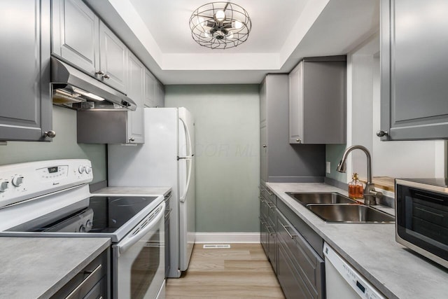 kitchen featuring sink, gray cabinetry, light hardwood / wood-style flooring, a raised ceiling, and white appliances